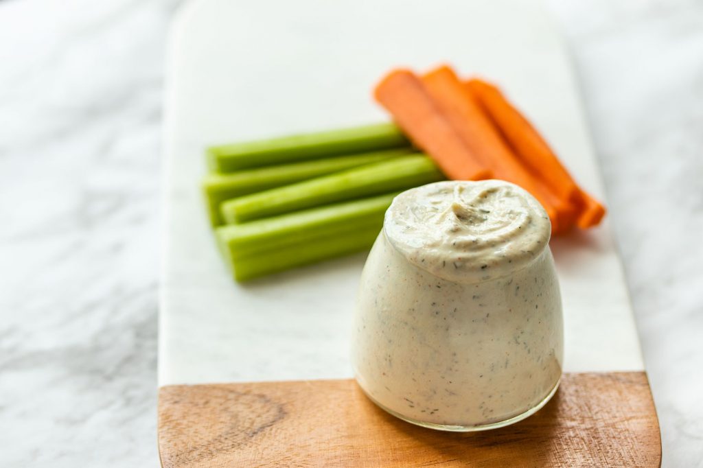 greek yogurt ranch dip in a small glass container with celery and carrots in the background