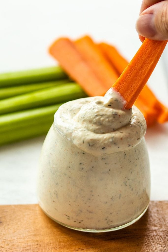 carrot being dunked into ranch dip with celery and carrot in the background