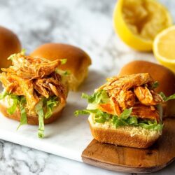 three buffalo chicken sliders on a marble serving tray with a cut lemon behind them