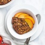 slice of vegan peaches and cream baked oatmeal on a white plate with two peach slices