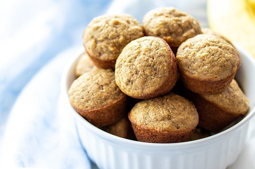 Mini Banana Muffins piled up in a white bowl next to a blue towel
