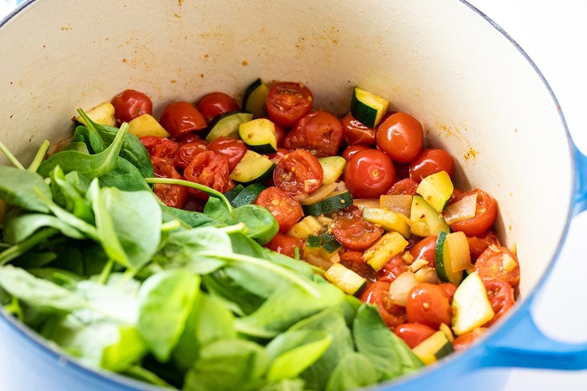 Sauteed tomato and zucchini with fresh spinach in a blue dutch oven