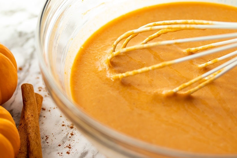Pumpkin puree, mashed banana, milk, eggs and vanilla being whisked in a glass bowl