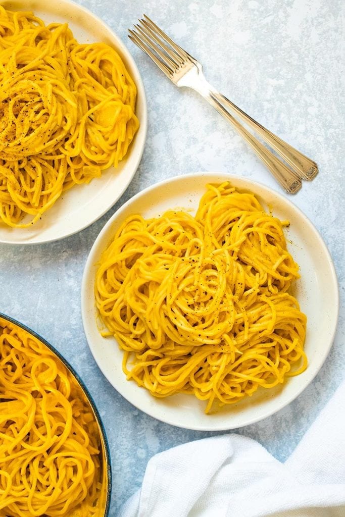 Two plates of spaghetti with butternut squash sauce viewed from overhead, next to a white towel and two forks