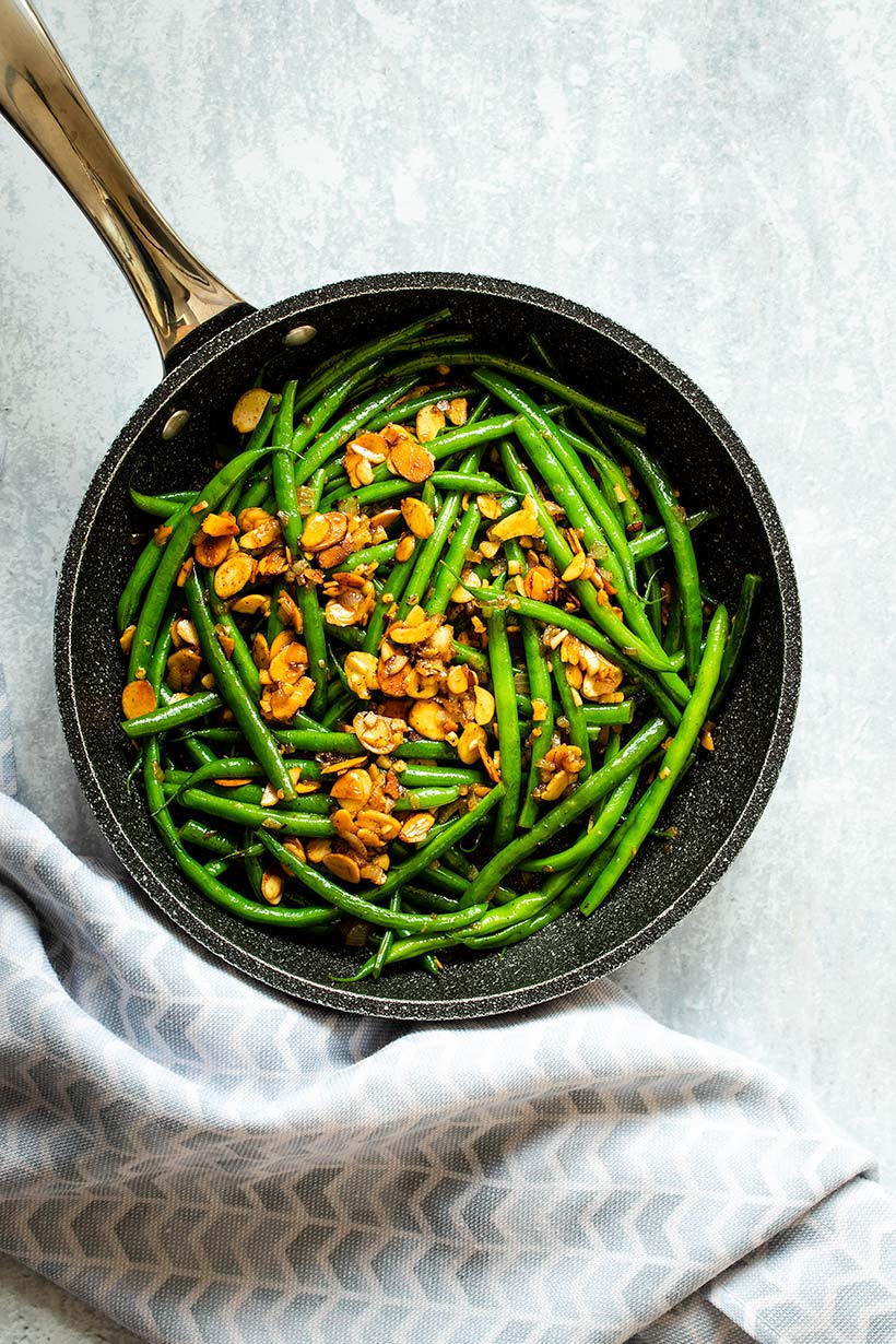Green beans almondine in a black skillet next to a blue and white towel