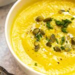 Instant Pot Cauliflower Soup in a white bowl topped with pumpkin seeds, pepper, olive oil and chives