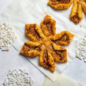 pesto and goat cheese snowflake pastry on parchment next to white and gold snowflake ornaments