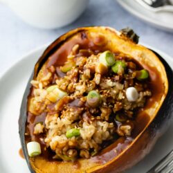 vegan stuffed acorn squash on a grey plate with a small white dish of miso maple gravy in the background