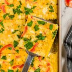 A slice of sheet pan omelette being lifted from the pan with a silver spatula.