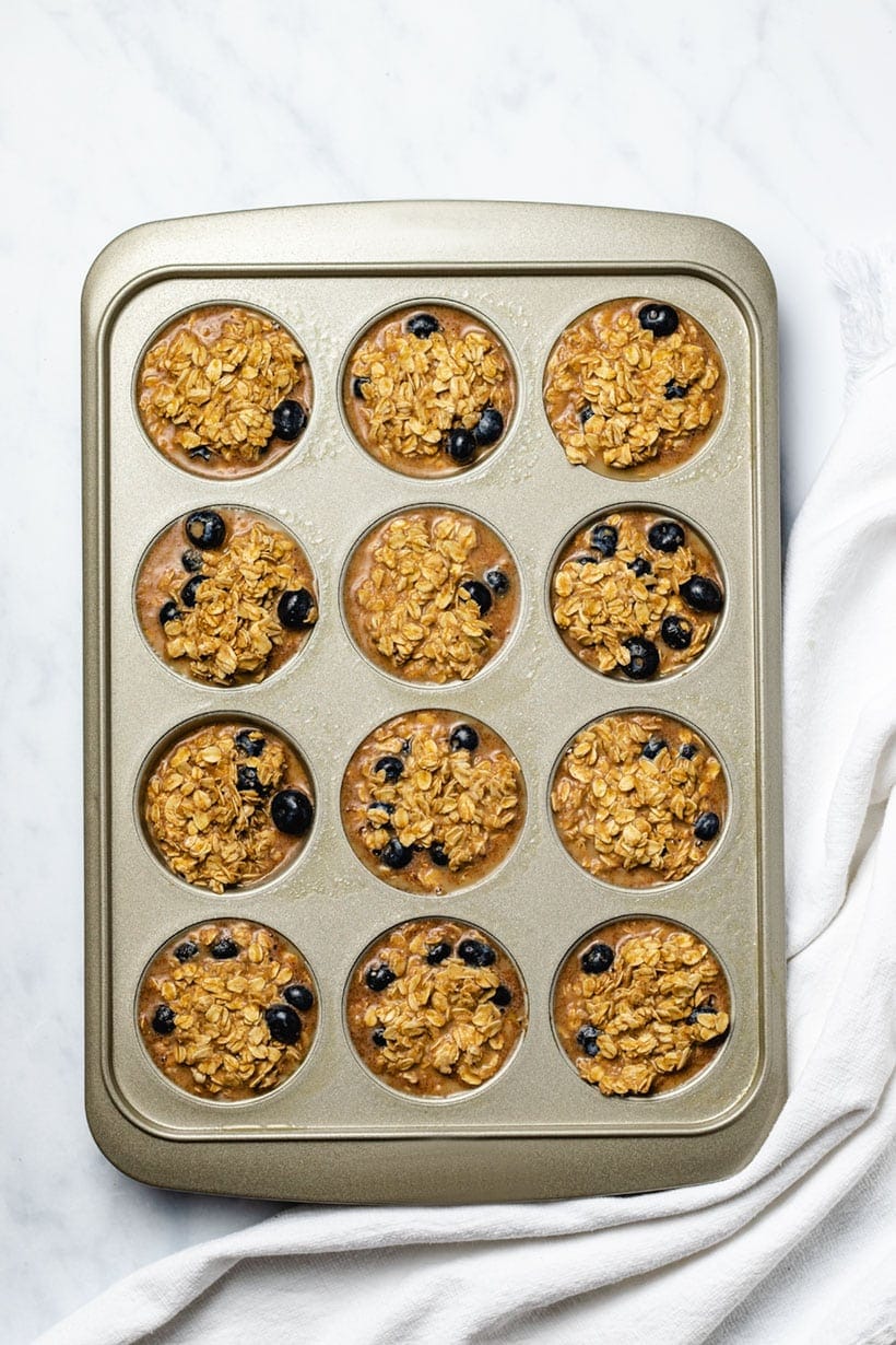 A muffin tin filled with oatmeal cup batter, next to a white linen