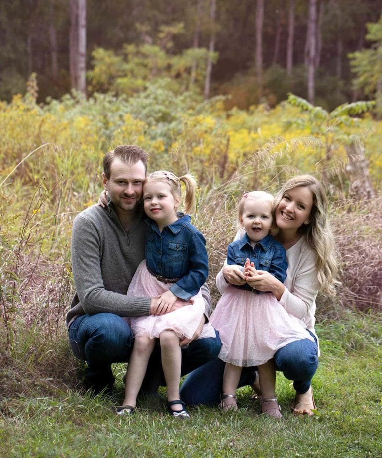 Laura and her husband and daughters in a field with yellow flowers in the background