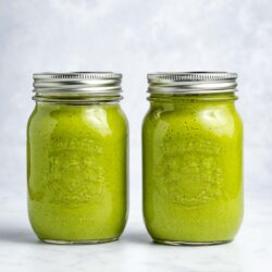 Two green smoothies in mason jars sitting side by side with a white background