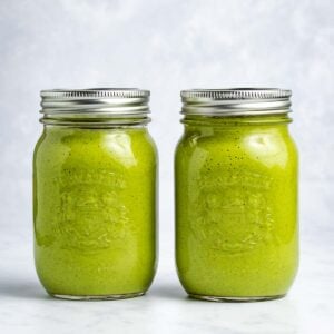 Two green smoothies in mason jars sitting side by side with a white background