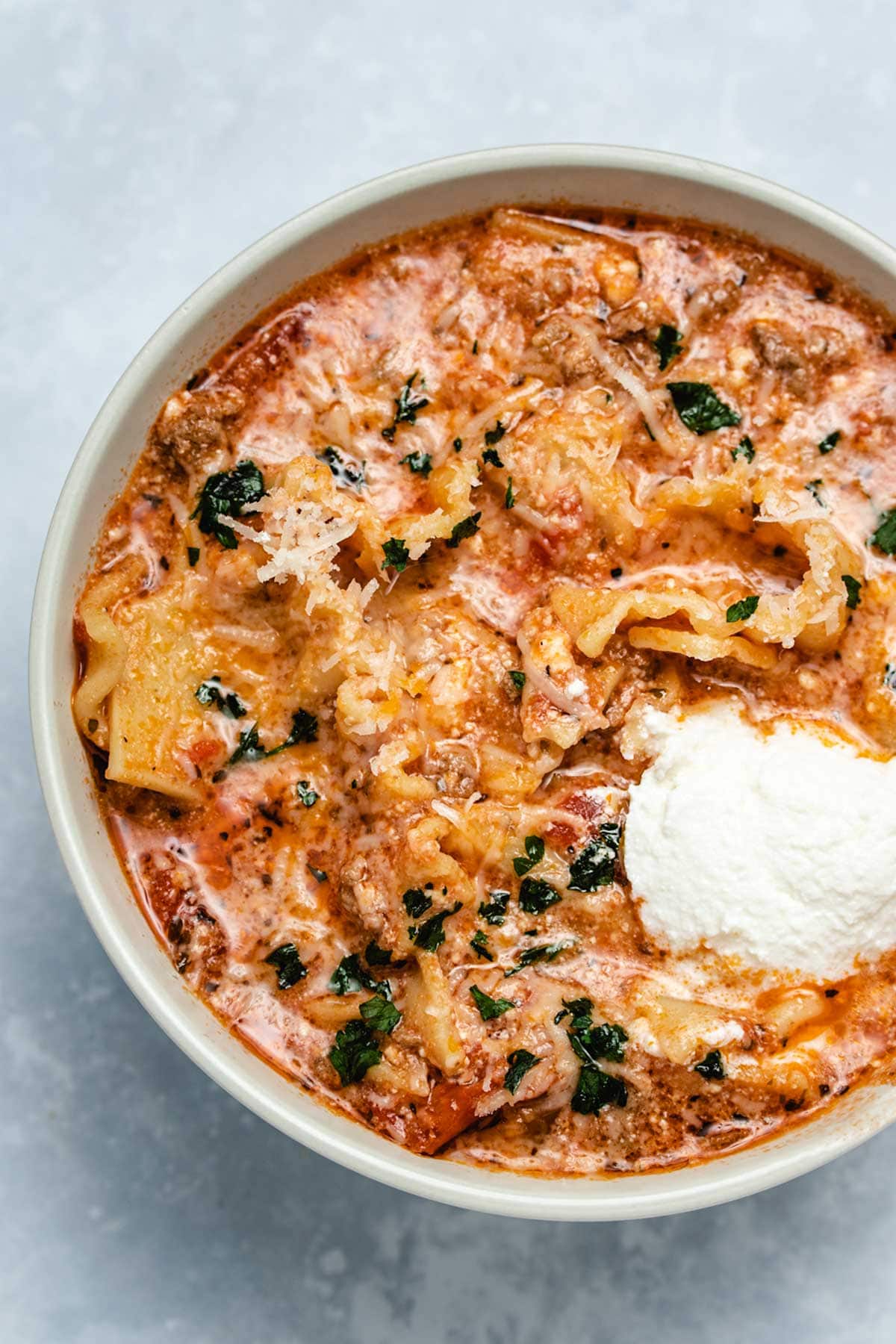 Lasagna soup in a beige bowl garnished with parsley and ricotta cheese viewed from overhead