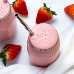 strawberry banana smoothie in a mason jar with a stainless steel straw with fresh strawberries in the background
