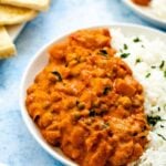 Potato and chickpea tikka masala with basmati rice on a white plate with sliced naan in the background