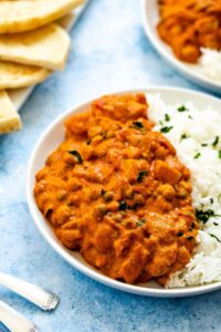 Potato and chickpea tikka masala with basmati rice on a white plate with sliced naan in the background