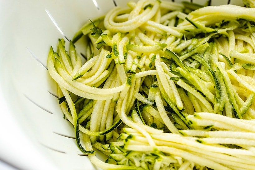 Salted grated zucchini in a white colander
