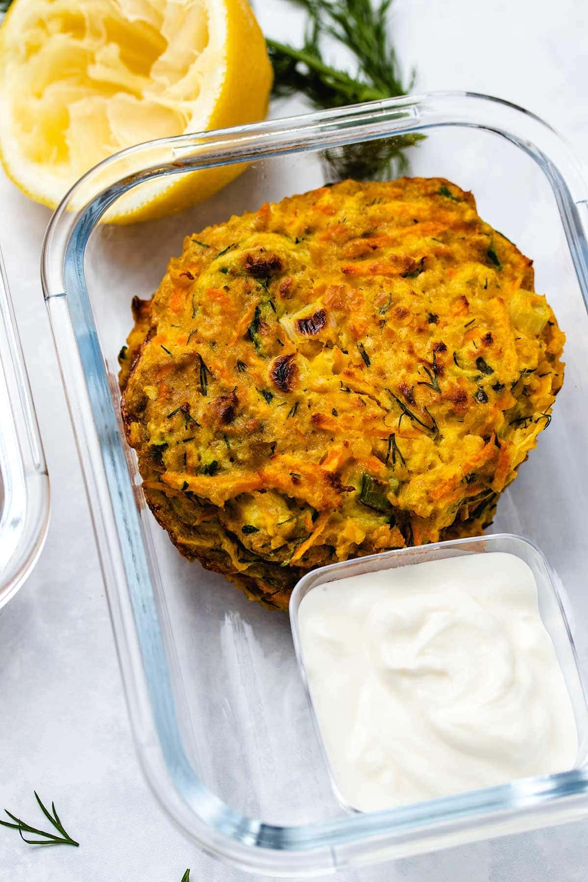 zucchini carrot fritters in a glass meal prep container with a side of greek yogurt