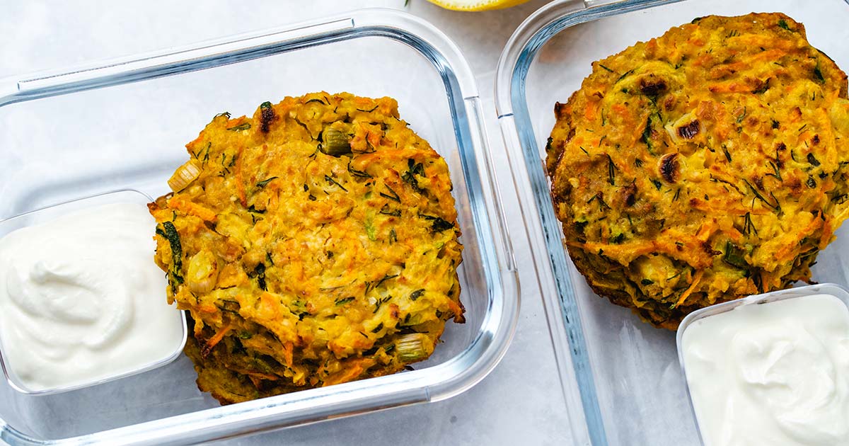 zucchini carrot fritters in 2 glass meal prep containers with a side of greek yogurt