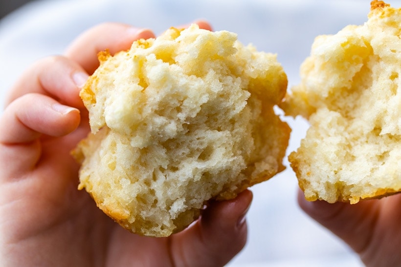 A biscuit muffin broken in half to show the texture, held by a child's hands