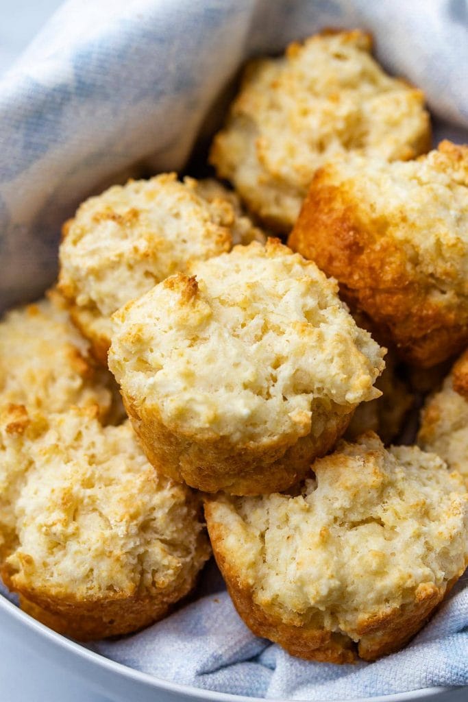 biscuit muffins piled up in a white bowl on top of a light blue linen