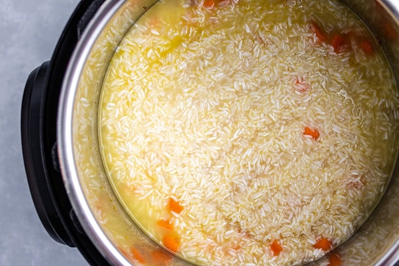 Uncooked rice and carrots submerged in broth in an Instant Pot
