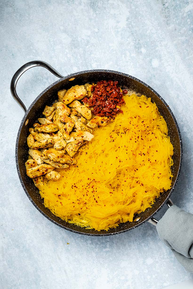 Sautéed chicken, chopped sundried tomato and spaghetti squash in a black skillet viewed from overhead