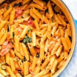 Creamy vegan one pot pasta with roasted red peppers and spinach in a blue dutch oven