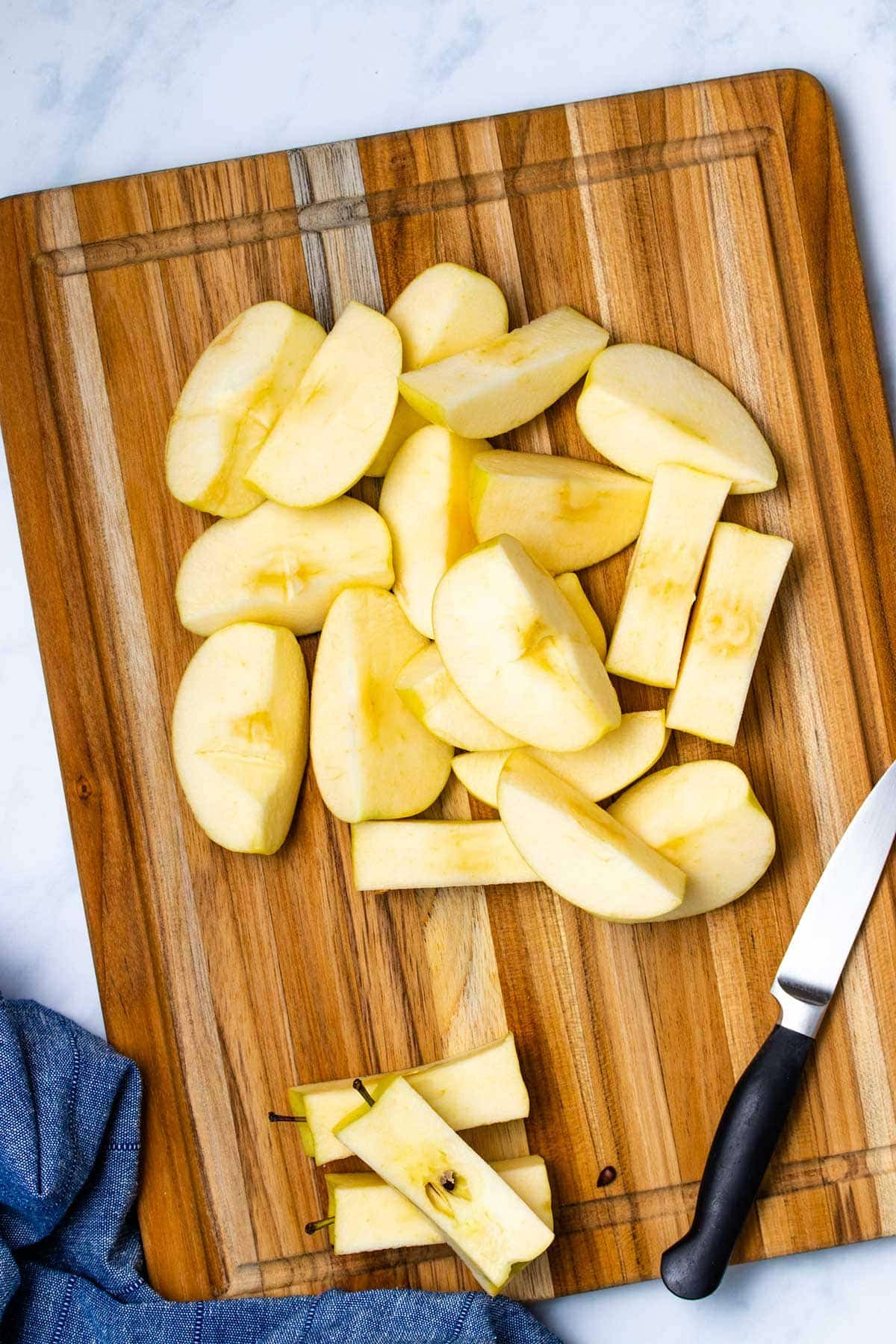 sliced apples on a wooden cutting board with a black-handled paring knife next to a blue linen