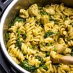 pesto chicken pasta in an Instant Pot being scooped by a wooden spoon