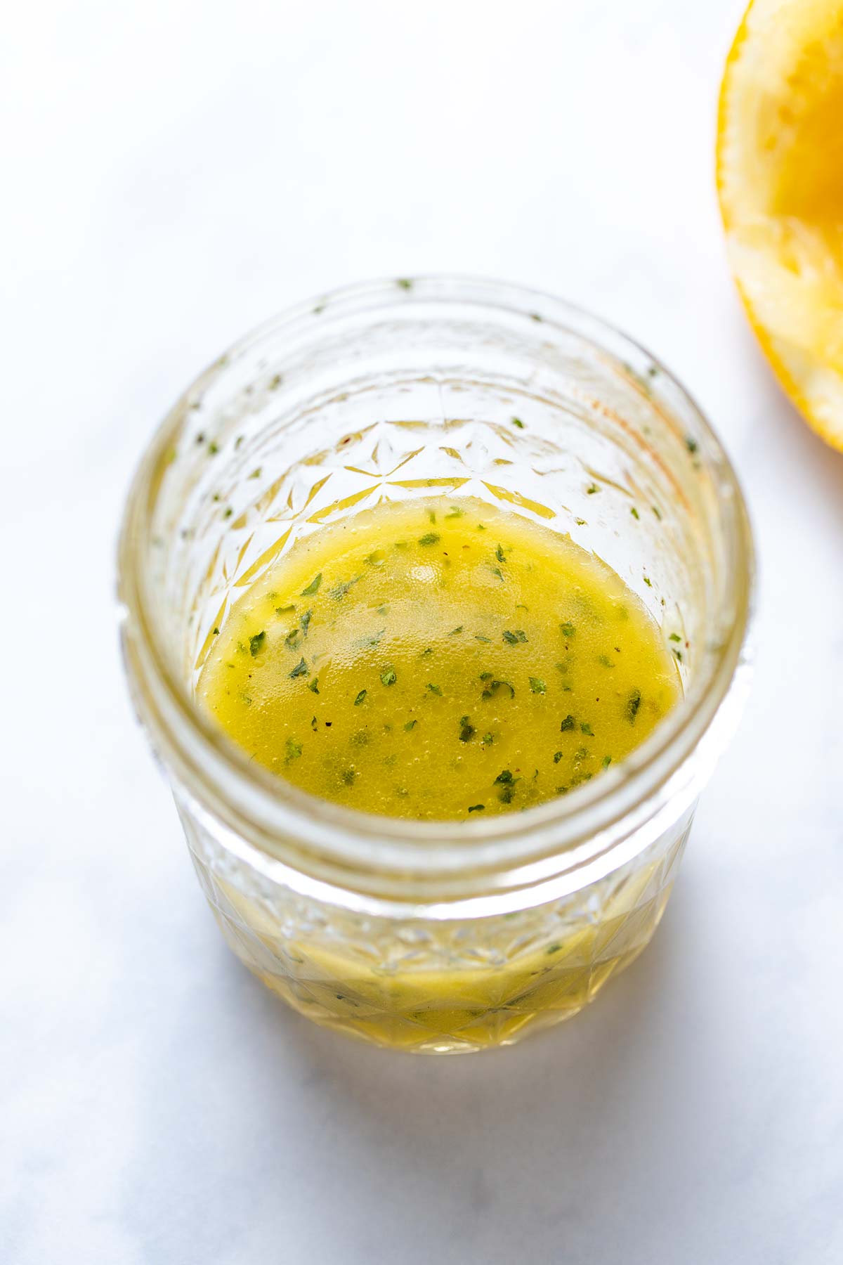 an olive oil and lemon dressing in a small mason jar next to half a squeezed lemon