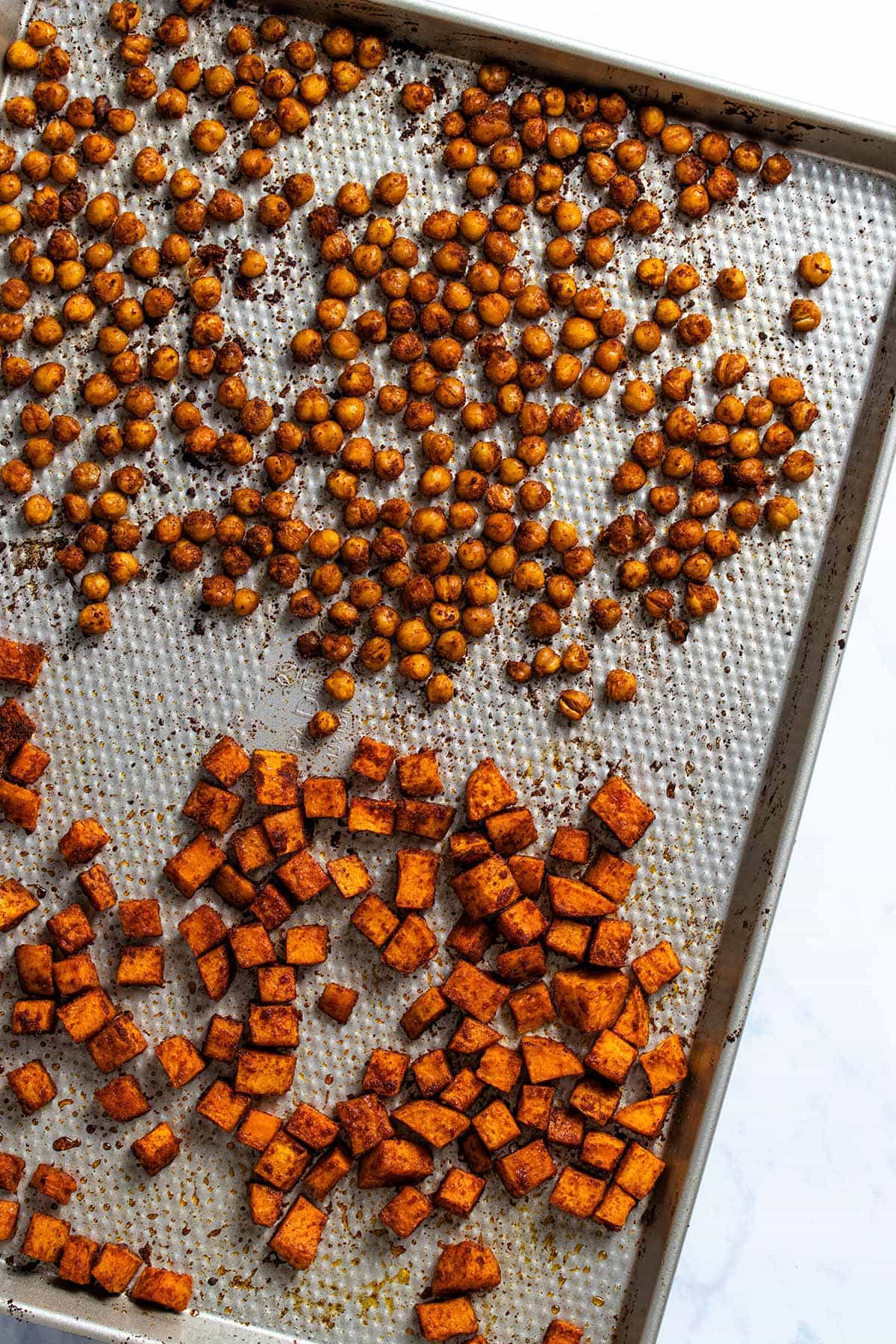 roasted chickpeas and diced sweet potato covered in moroccan spices on a silver sheet pan