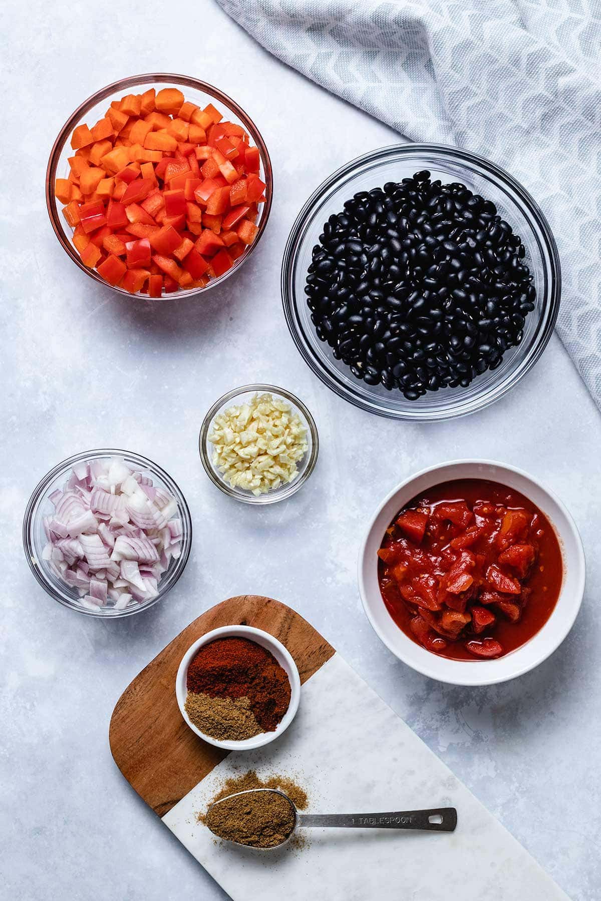 black bean soup ingredients in small bowls: diced carrots, red bell pepper, dried black beans, diced tomatoes, minced garlic, diced red onion and spices