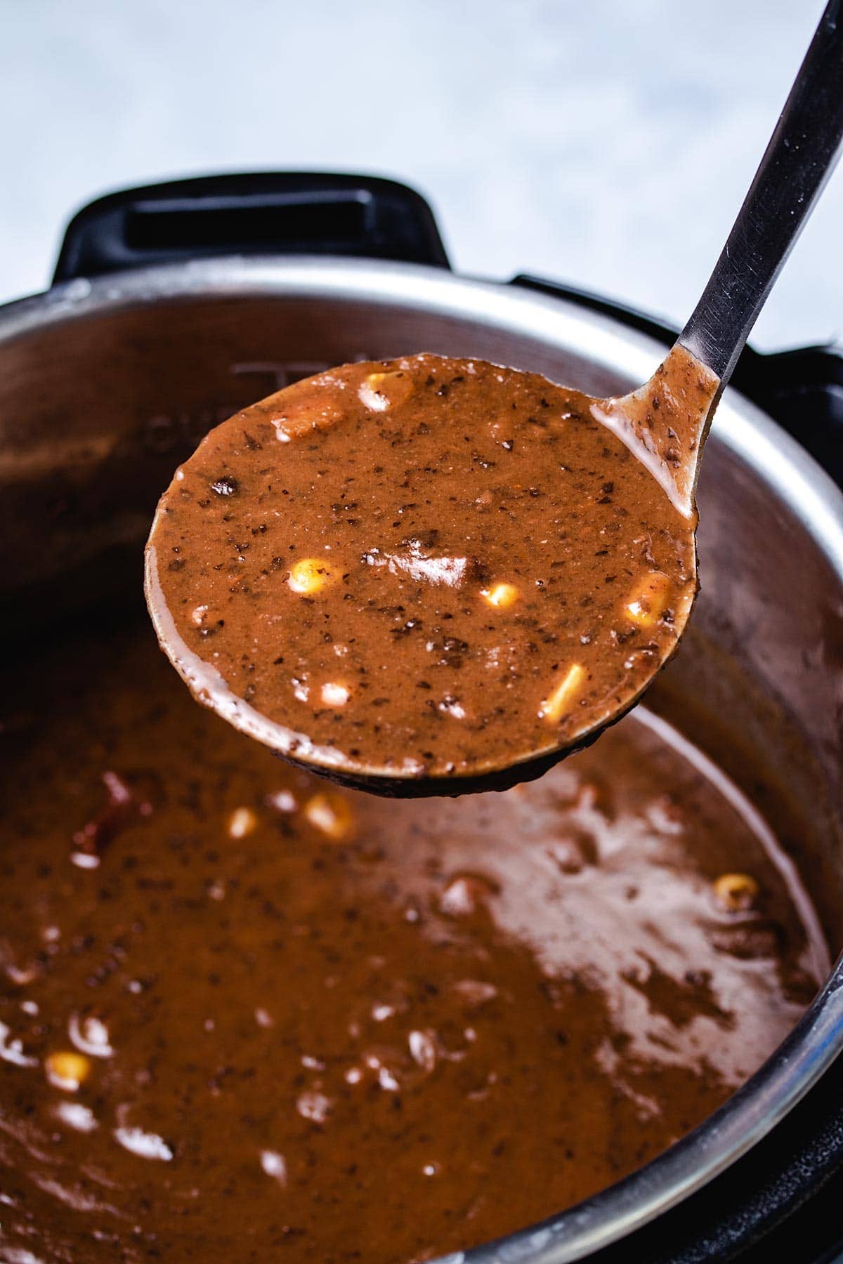 a ladle of black bean soup held over an Instant Pot filled with black bean soup