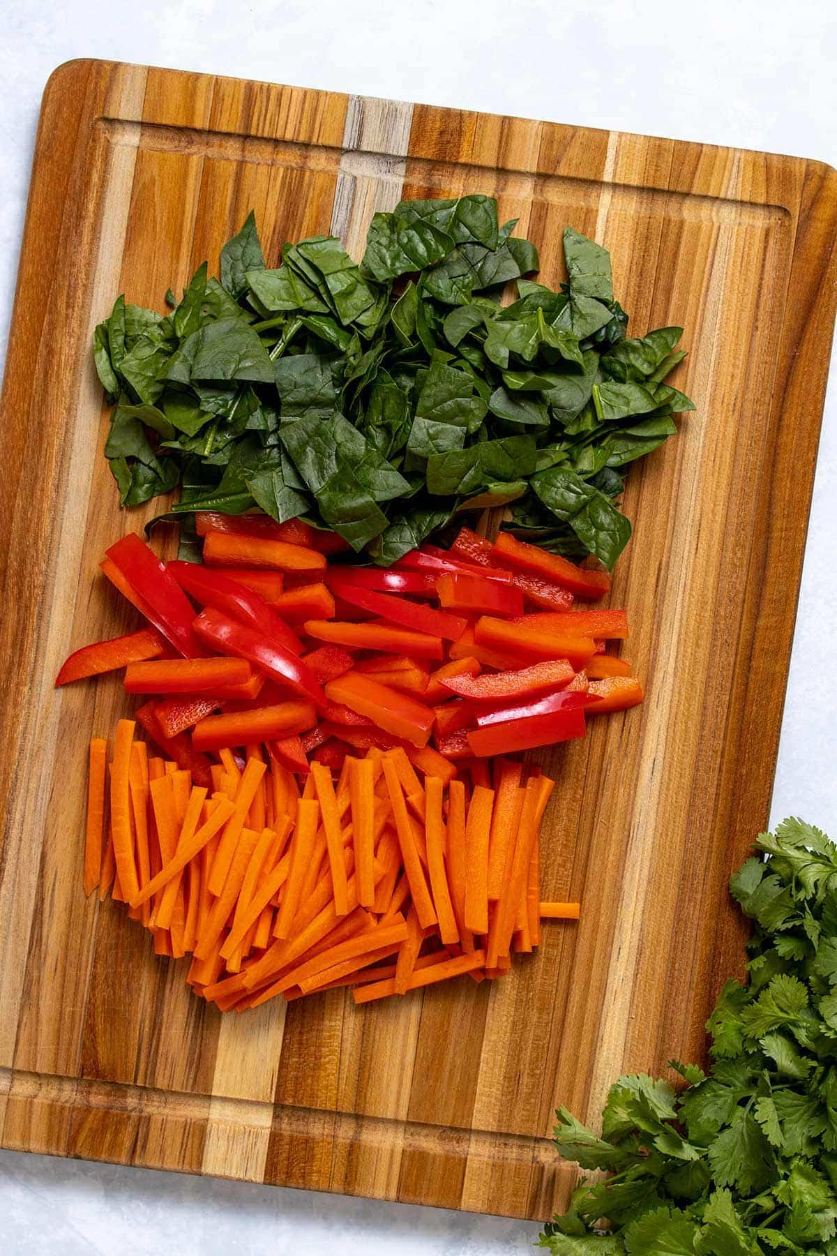 chopped baby spinach, sliced red bell pepper and matchstick carrots on a wooden cutting board