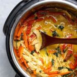 Thai chicken curry in an Instant Pot being scooped with a wooden spoon