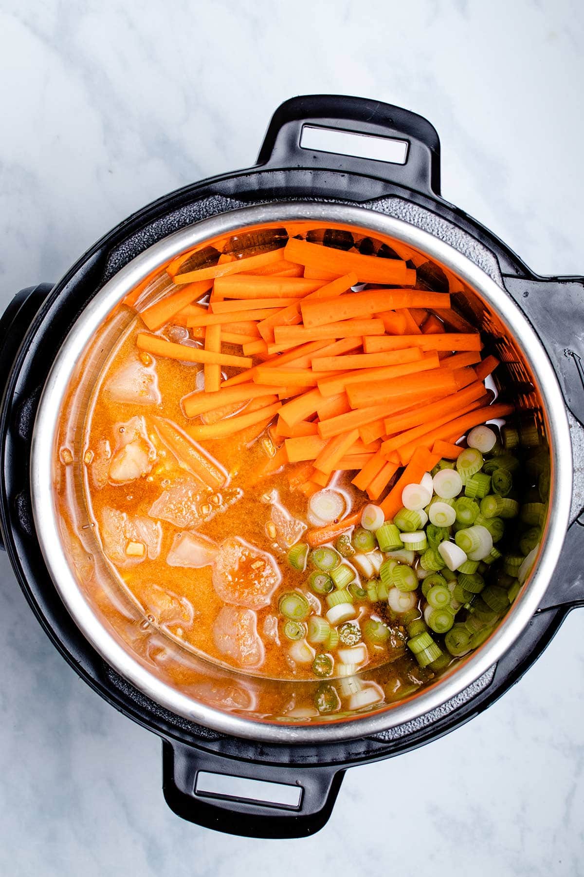 Diced chicken breast, homemade pad Thai sauce, sliced green onion and matchstick carrots in an Instant Pot viewed from overhead
