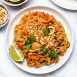 Instant Pot Chicken Pad Thai on a white plate garnished with cilantro, chopped peanuts and a lime wedge