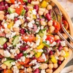 Mediterranean Bean Salad in a wooden bowl with two silver serving spoons resting in the right side of the salad.