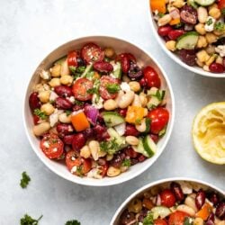 Mediterranean Bean Salad in 3 white bowls next to a squeezed lemon half and fresh herbs
