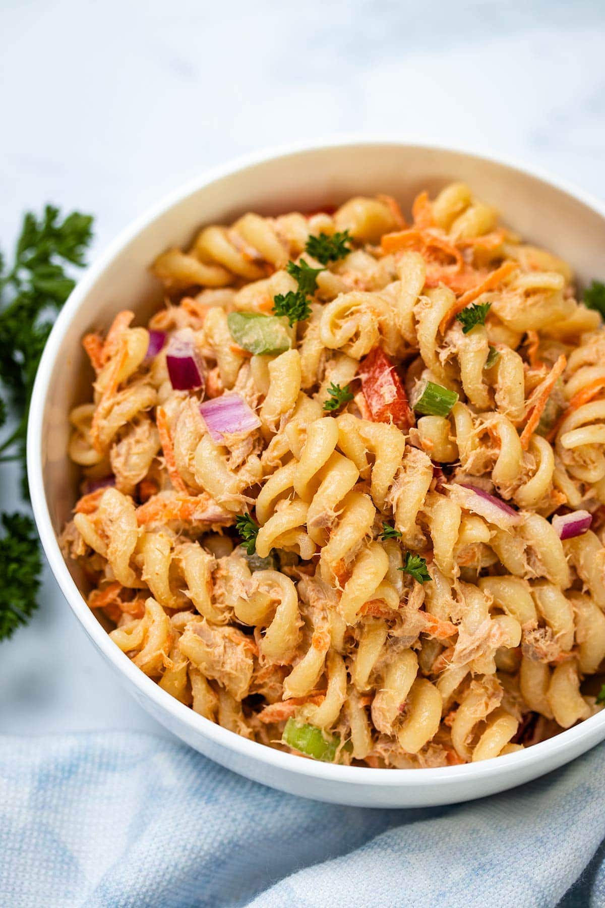 A closeup of Spicy Tuna Pasta Salad in a white bowl next to a blue linen