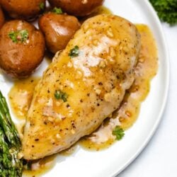 a chicken breast with lemon garlic sauce next to potatoes and asparagus on a white plate