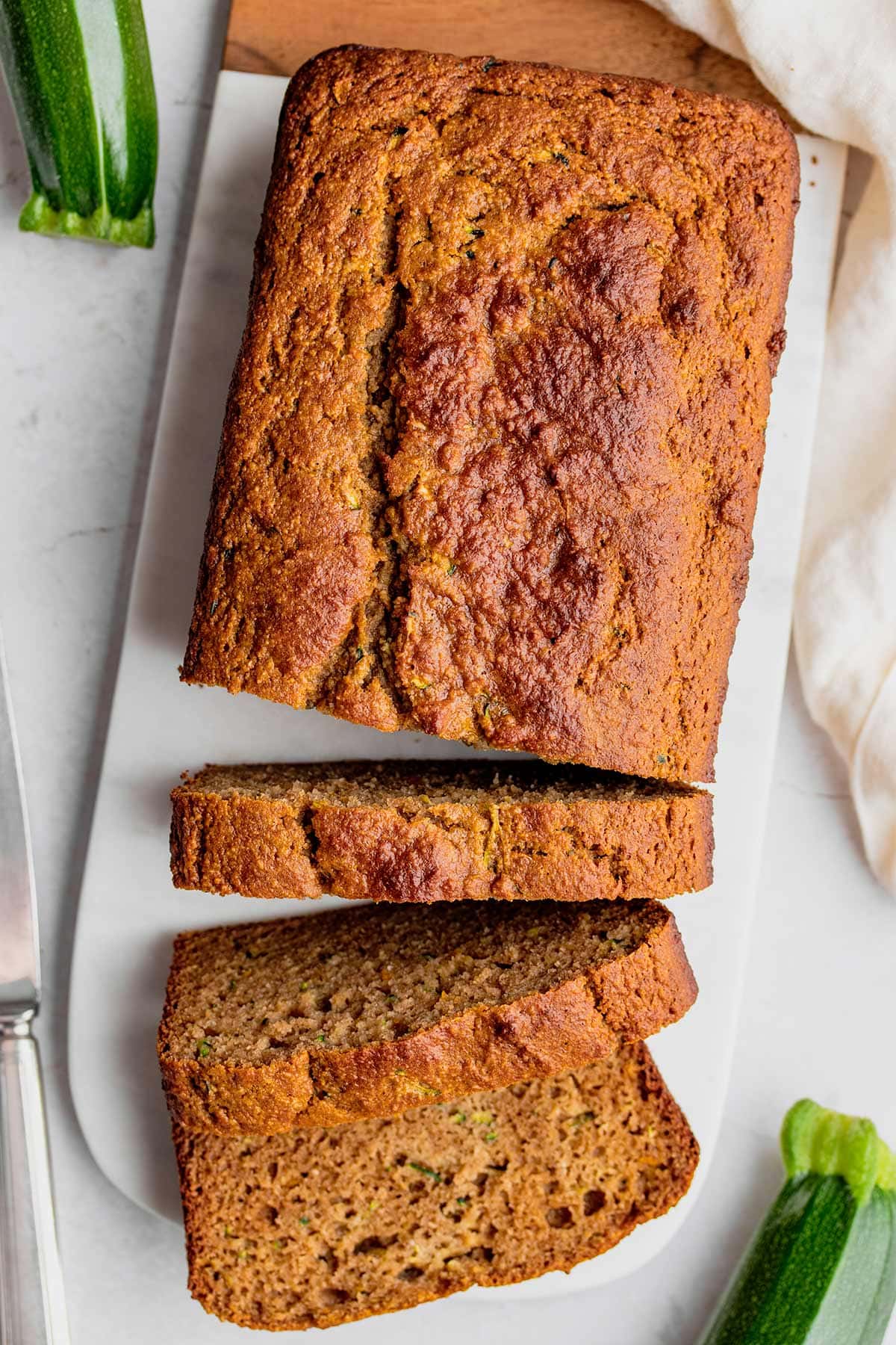 A loaf of almond flour zucchini bread being sliced on a marble serving tray