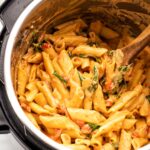 creamy vegan pasta with spinach and roasted red peppers being stirred by a wooden spoon in an Instant Pot