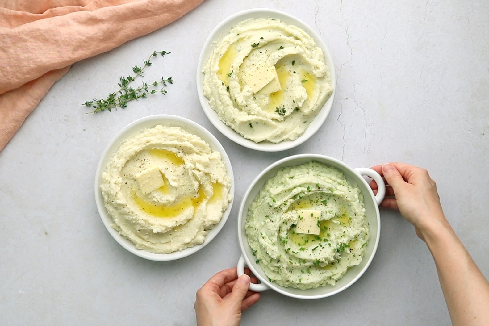 Two hands placing a third plate of mashed cauliflower next to two plates with different flavours.