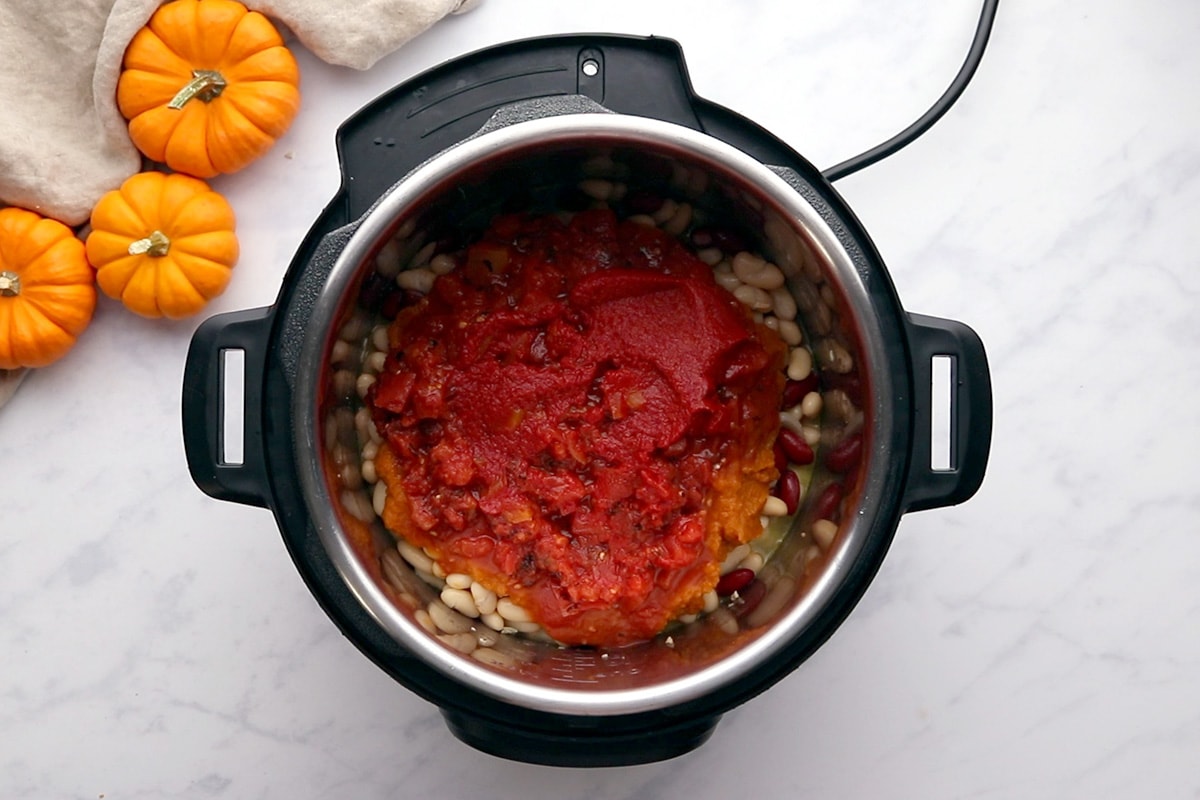 Pumpkin purée, tomatoes and tomato paste layered on top of kidney beans in an Instant Pot.