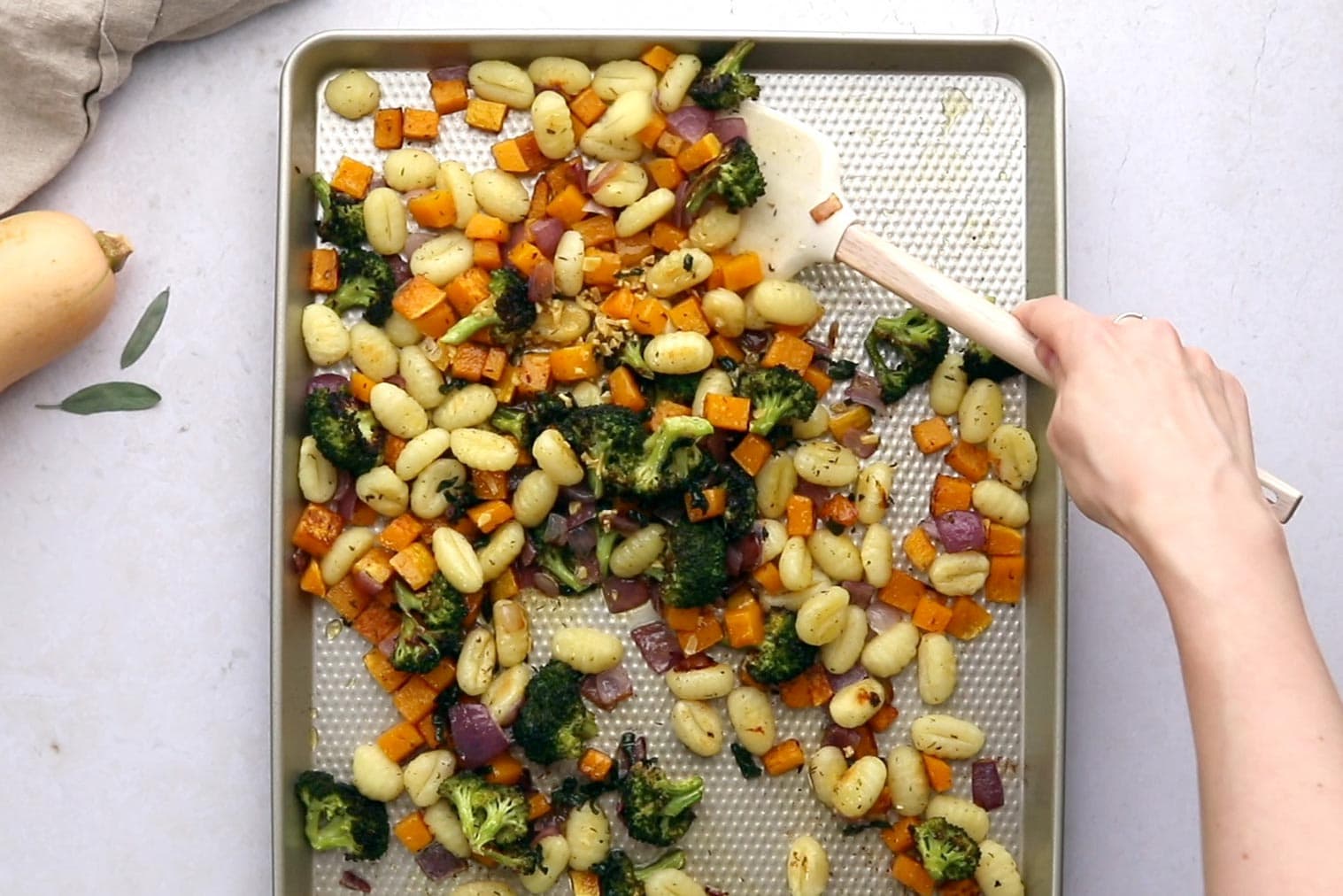tossing sheet pan gnocchi and vegetables in brown butter sage sauce using a white spatula
