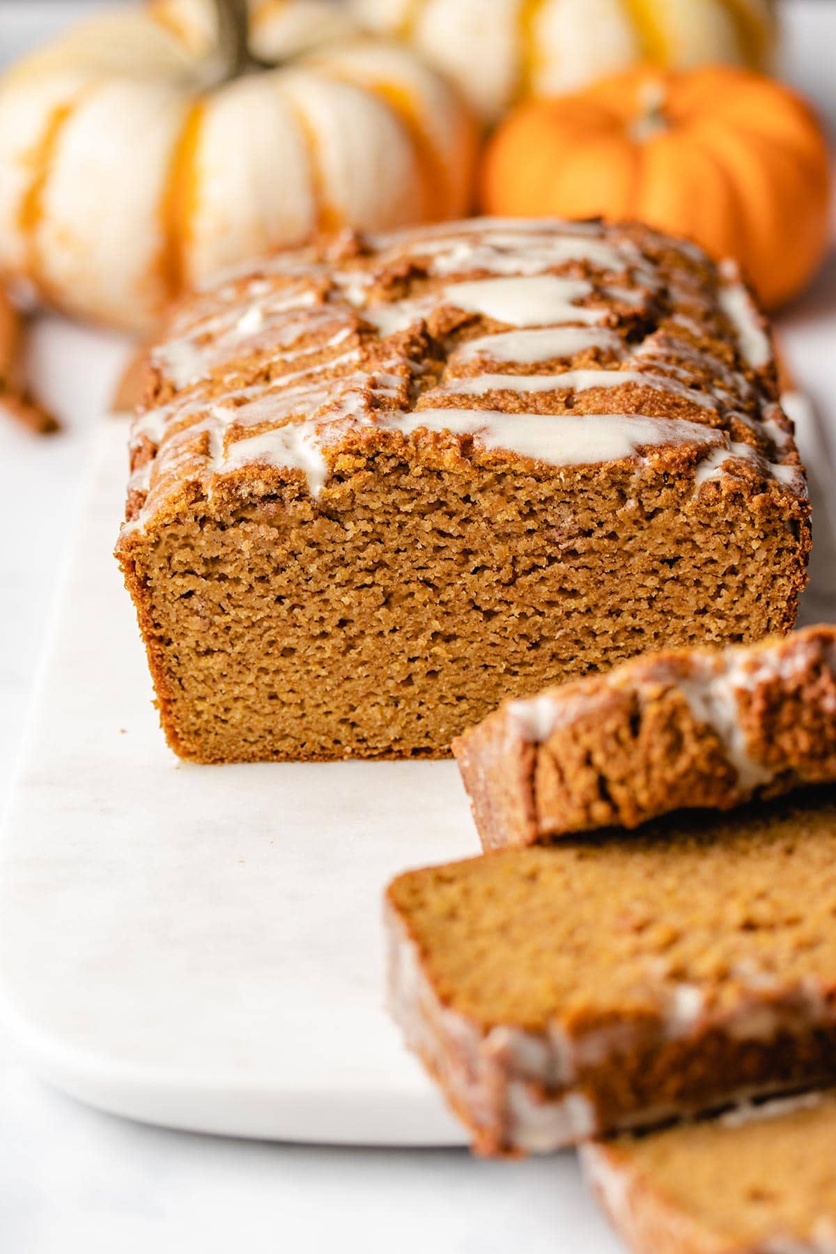 A cut loaf of almond flour pumpkin bread viewed head on with pumpkins in the background.