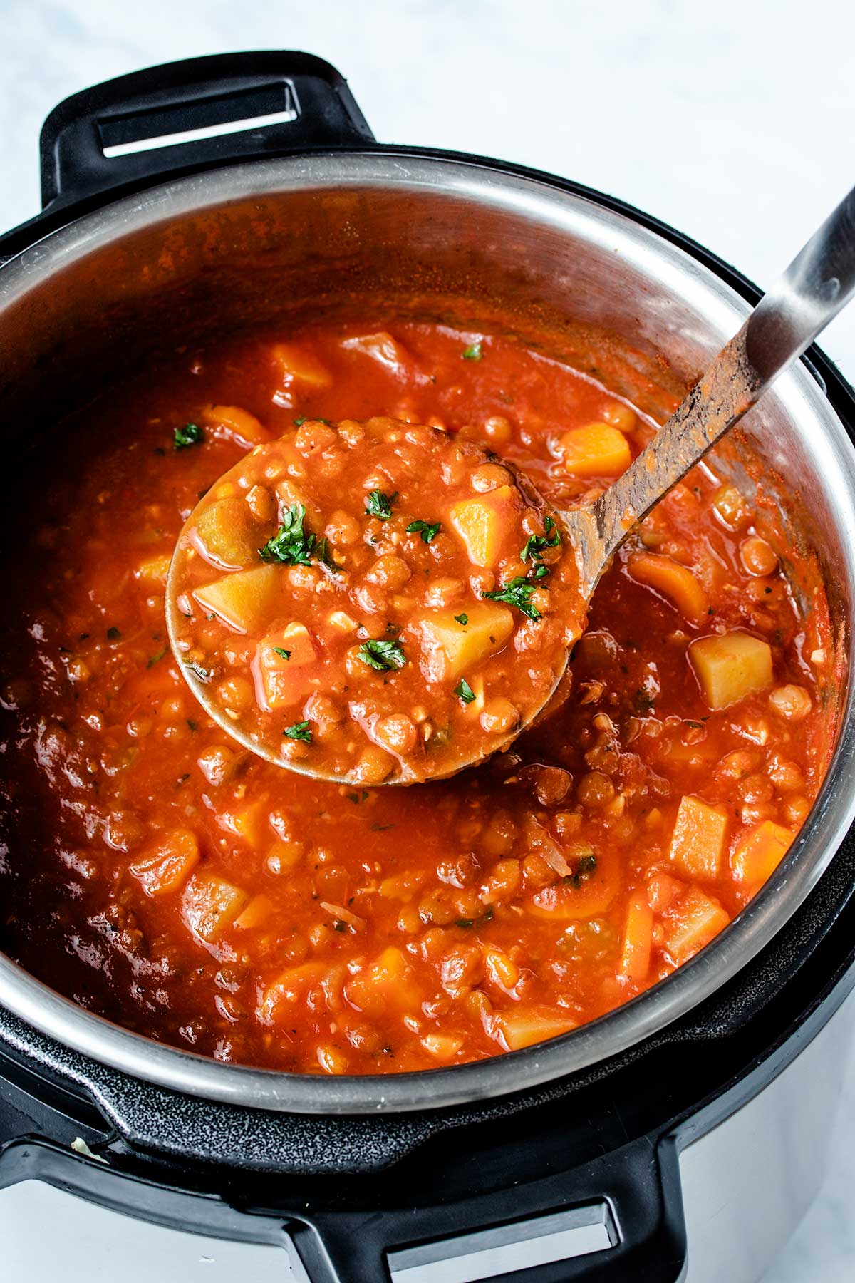 A ladle full of lentil soup being held over an Instant Pot.